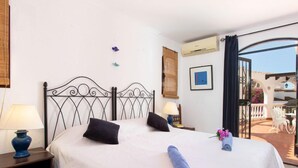 A hotel room with a bed, two bedside tables, a window with curtains, a wall-mounted air conditioner, and a balcony with outdoor furniture. - Cecilie by Interhome (Nerja)