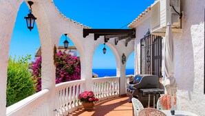 A covered outdoor patio with white railings, a grill, and a view of the sea. - Cecilie by Interhome (Nerja)