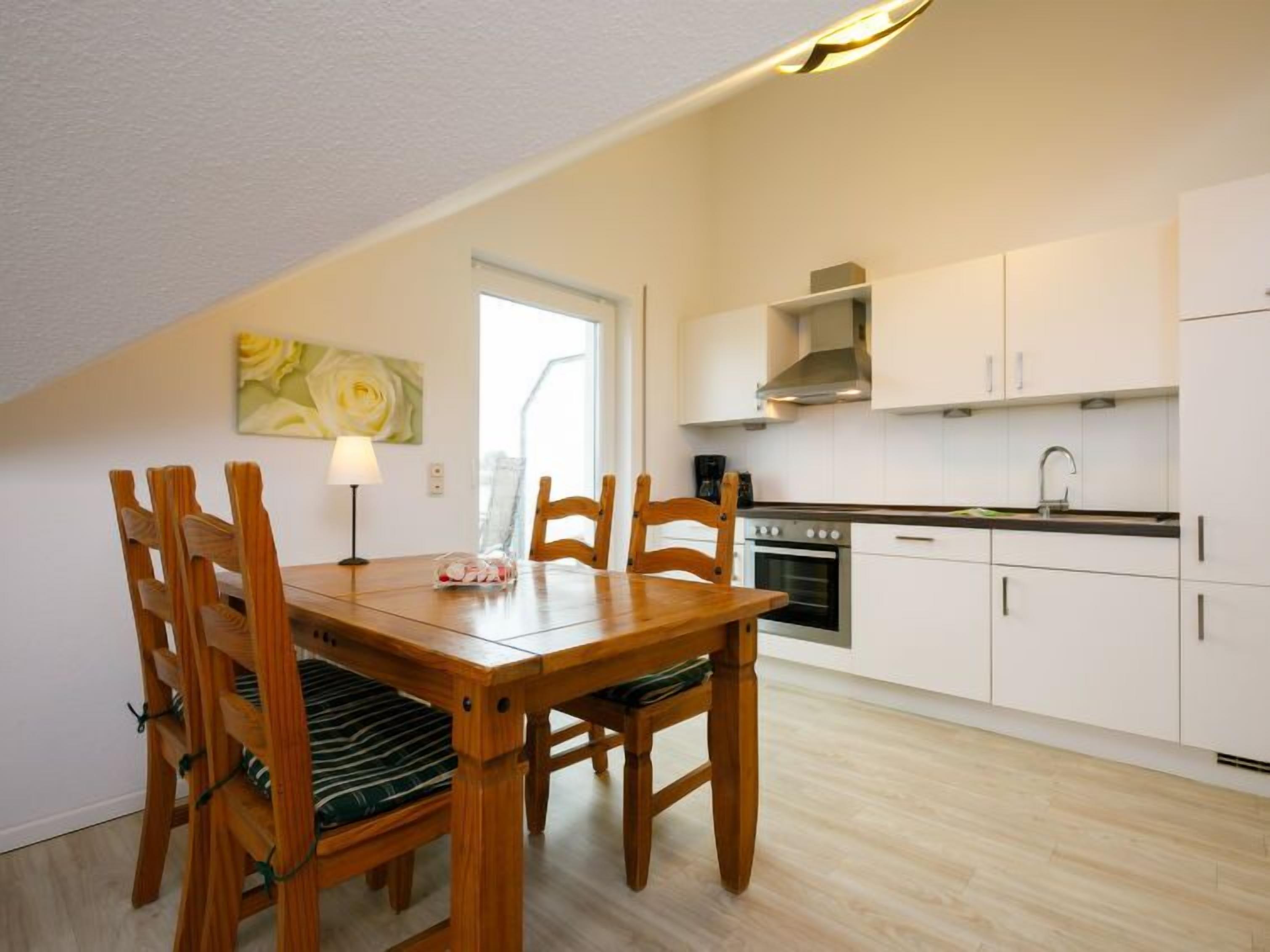 A dining area with a wooden table and chairs, a lamp, and a kitchen with white cabinets and a stove.