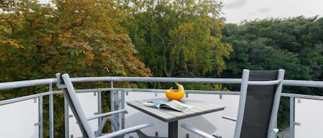Een balkon met een tafel en twee stoelen, een gele schaal met fruit en een boek.