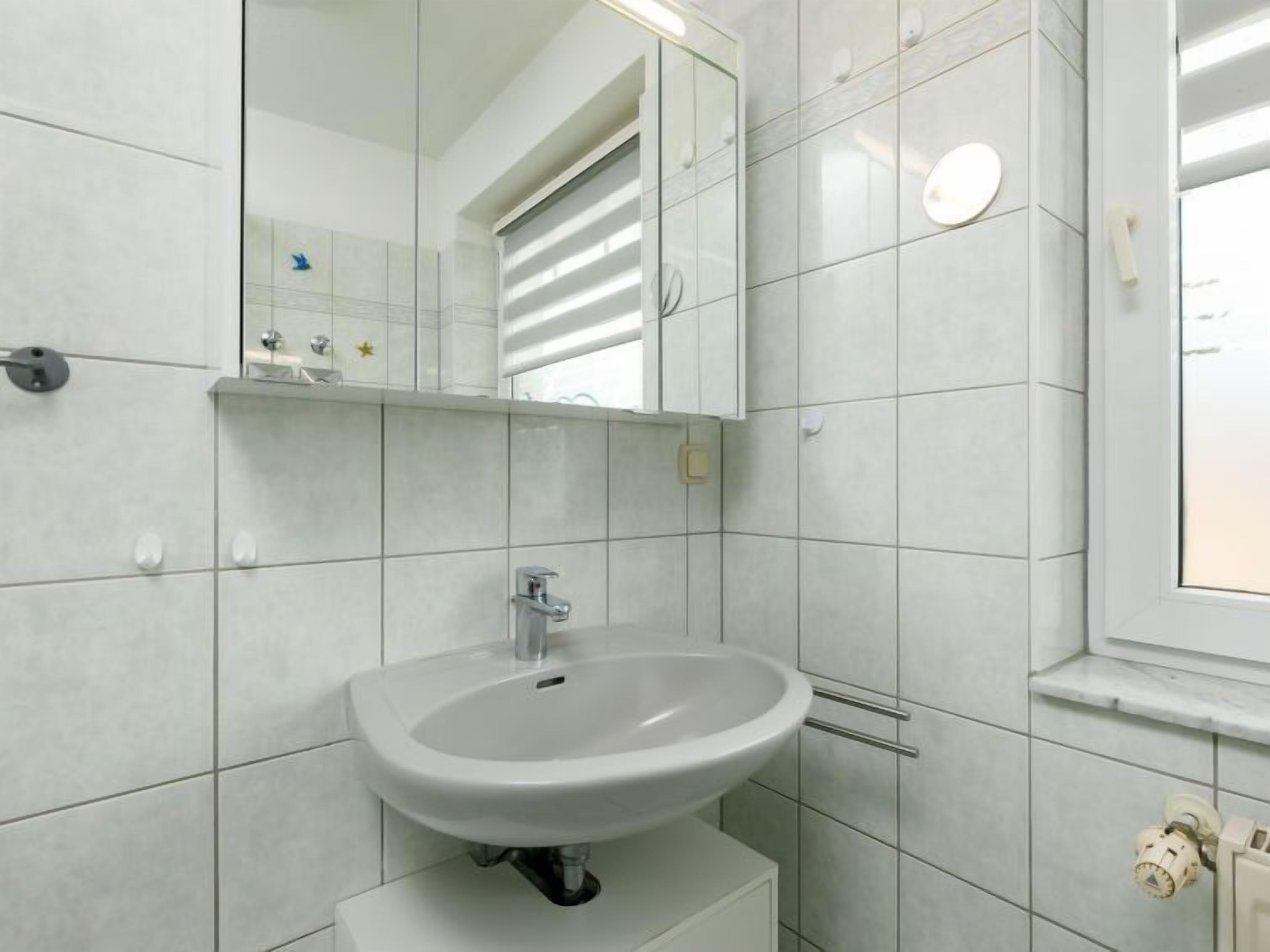 A bathroom with a white sink, mirror, and tiled walls.