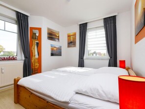 A bedroom with a wooden bed, white bedding, a red lamp, and a window with curtains. - Schwarz by Interhome (Koserow)