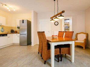 A modern kitchen with white cabinets, a stainless steel refrigerator, and a dining area with wicker chairs and a wooden table. - Apartment Neptun by Interhome (Koserow)