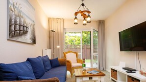 Una sala de estar acogedora con un sofá, una silla de mimbre, una mesa de centro y un televisor.