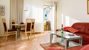 Een woonkamer met een glazen salontafel, een rode bank en houten stoelen. Er is een eethoek met een tafel en stoelen, en zicht op een gebouw buiten.