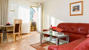 Een woonkamer met een glazen salontafel, een rode leren bank en een eethoek met een tafel en stoelen.