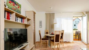 Een woonkamer met een flatscreen televisie, een boekenkast, een eettafel met stoelen en een vloer met zeshoekig tegels.