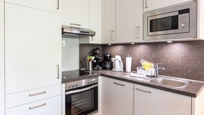 Uma cozinha compacta com armários brancos, forno embutido, micro-ondas e cafeteira.