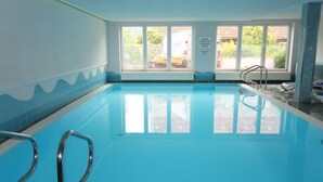 Piscina interior com paredes de vidro transparente, chão ladrilhado e entrada com janelas.