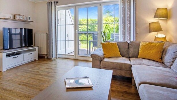 Uma sala de estar com sofá, mesa de centro, televisão e porta de vidro deslizante que dá para uma varanda.