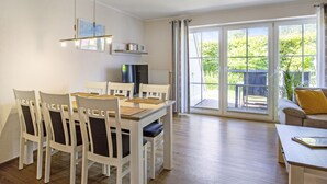 Uma área de refeições com mesa e cadeiras, um sofá e vista para o exterior por grandes janelas.