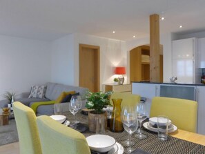 Un salon moderne avec un coin repas, comprenant un canapé, des fauteuils jaunes, une table dressée et une cuisine en arrière-plan.