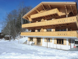 Un chalet en bois à plusieurs étages, doté de balcons, niché dans un paysage enneigé.