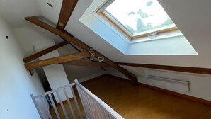 Una habitación con techos altos, vigas de madera a la vista, tragaluces y una escalera de madera.