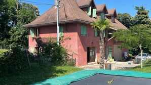 Una casa de dos pisos con fachada de ladrillo rojo, techo verde y un trampolín en el jardín delantero.