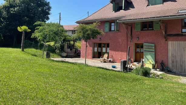 Una casa de dos pisos con fachada de ladrillo rojo, contraventanas verdes y techo inclinado.