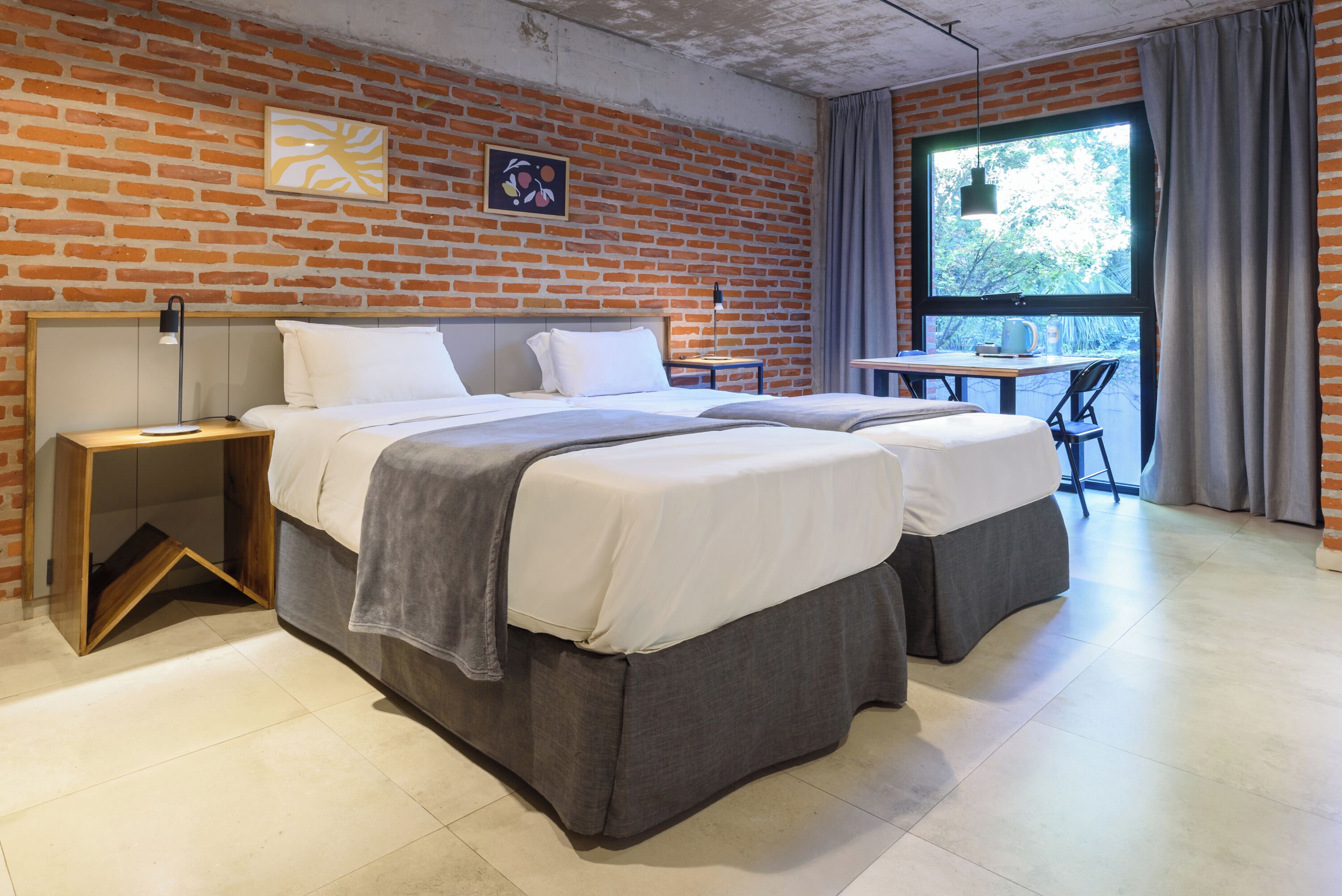 Ein modernes Zimmer mit Backsteinwand, zwei Betten, einem Schreibtisch und einem großen Fenster.
