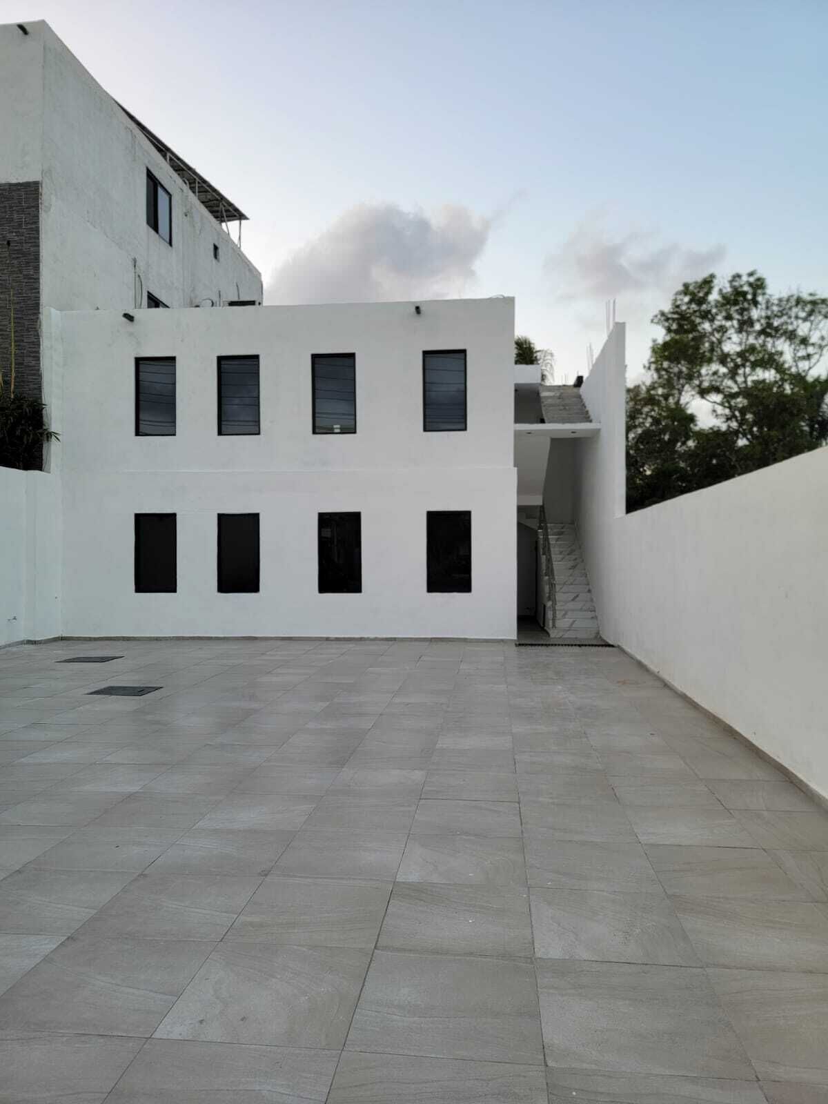 A modern building with a flat roof, large windows, and a paved courtyard.