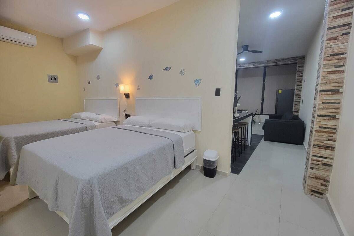 A hotel room with two beds, a small kitchenette, and a dining area.