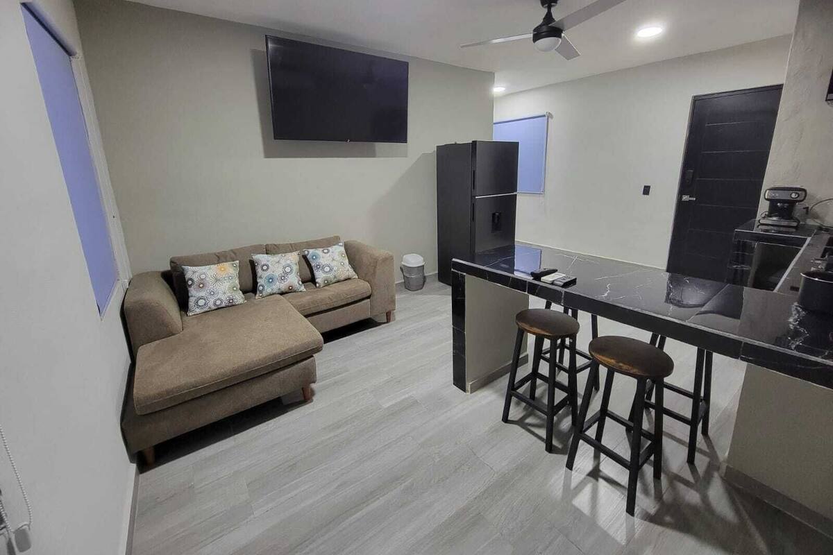 A compact living space with a sofa, a small kitchen area, and a ceiling fan.