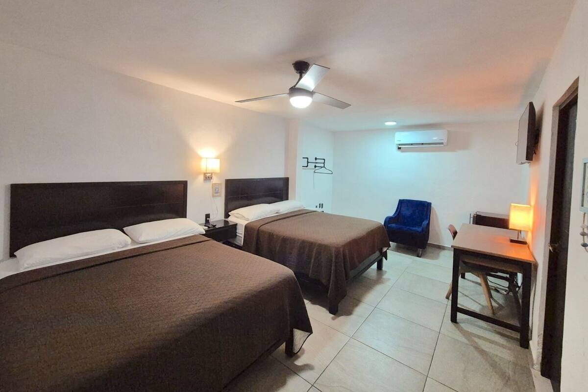 A hotel room with two beds, a ceiling fan, a desk with a chair, and a TV mounted on the wall.