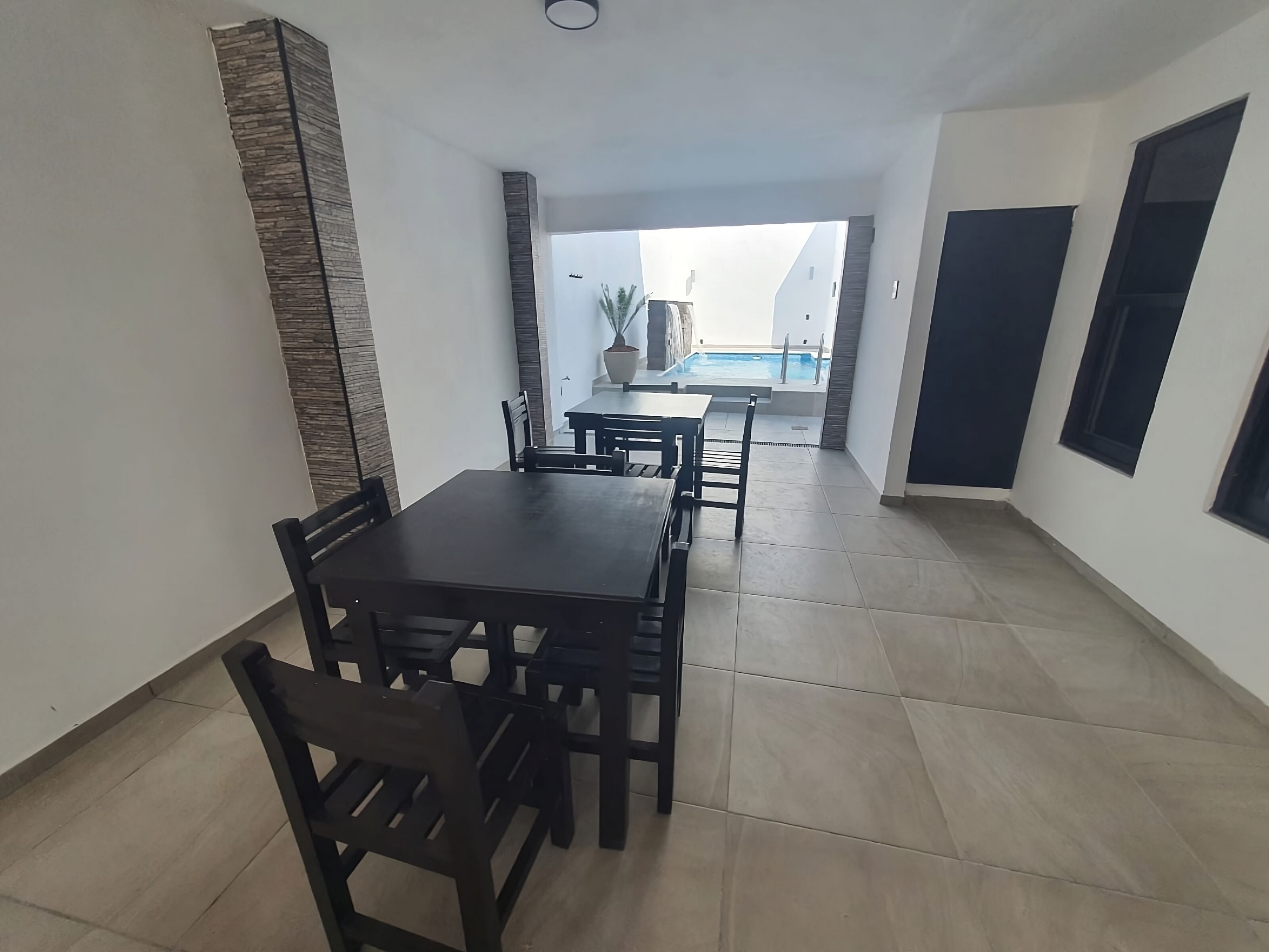 Un espace repas comprenant une table et des chaises, un sol carrelé et une vue sur une piscine en arrière-plan.