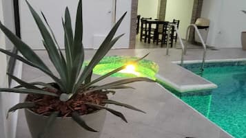 Un área de piscina con una planta en maceta, una mesa junto a la piscina y una silla.