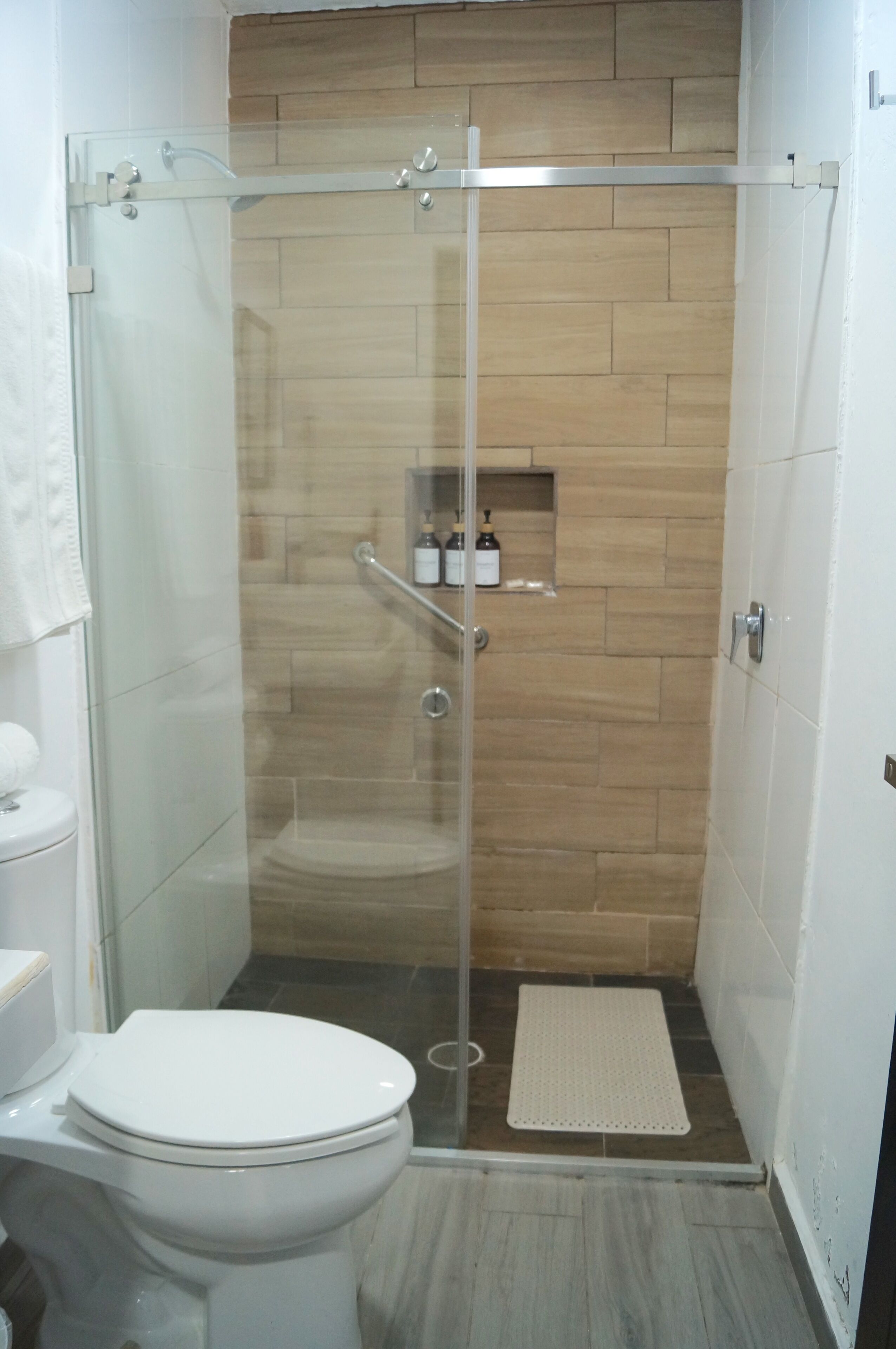 A small, enclosed shower area with a glass door, a toilet, and a shelf with toiletries.