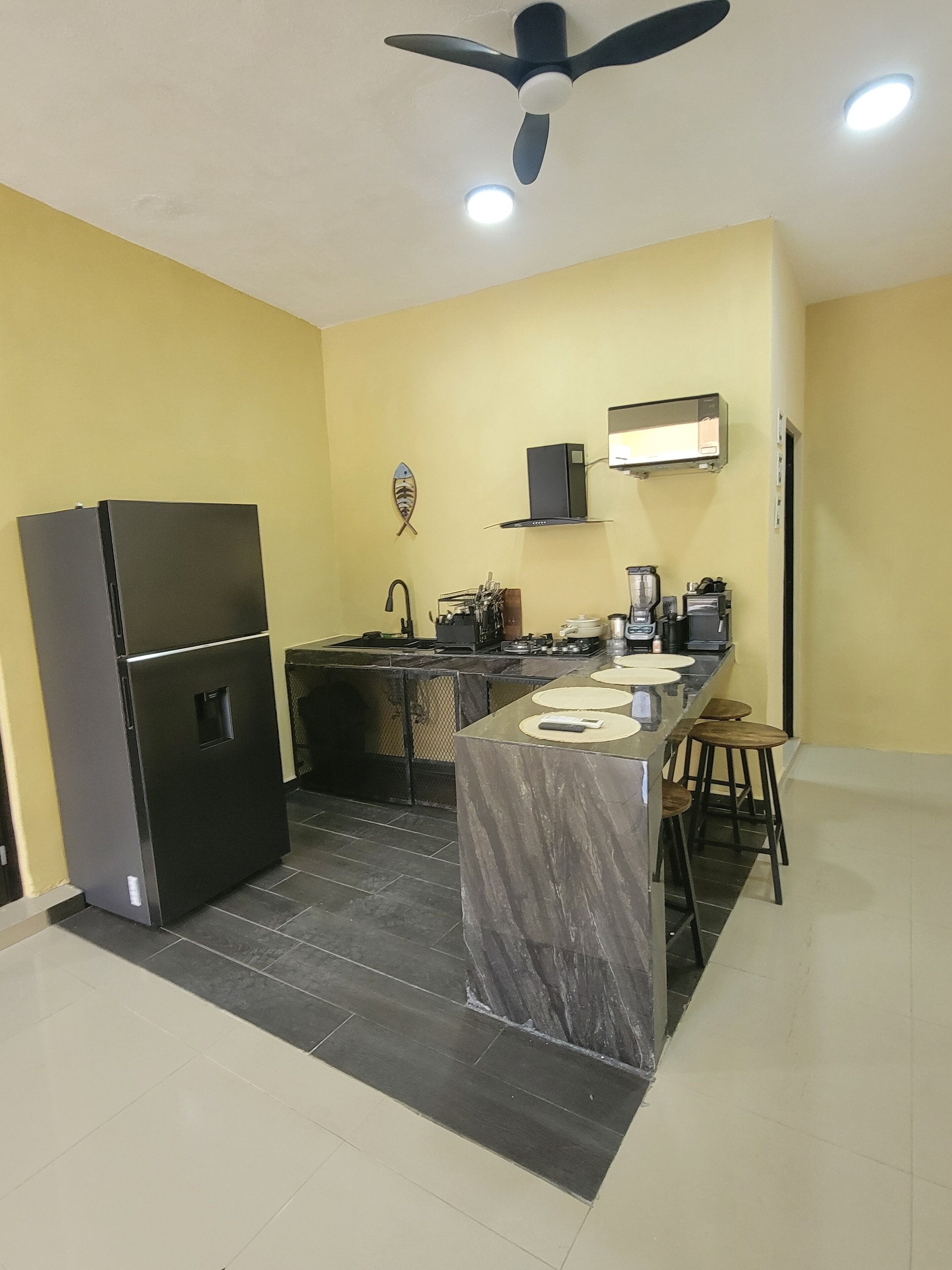 Cocina compacta con refrigerador, estufa, lavamanos y ventilador de techo.