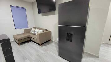 Una sala de estar moderna con un sofá modular, un televisor de pantalla plana y un refrigerador negro grande.