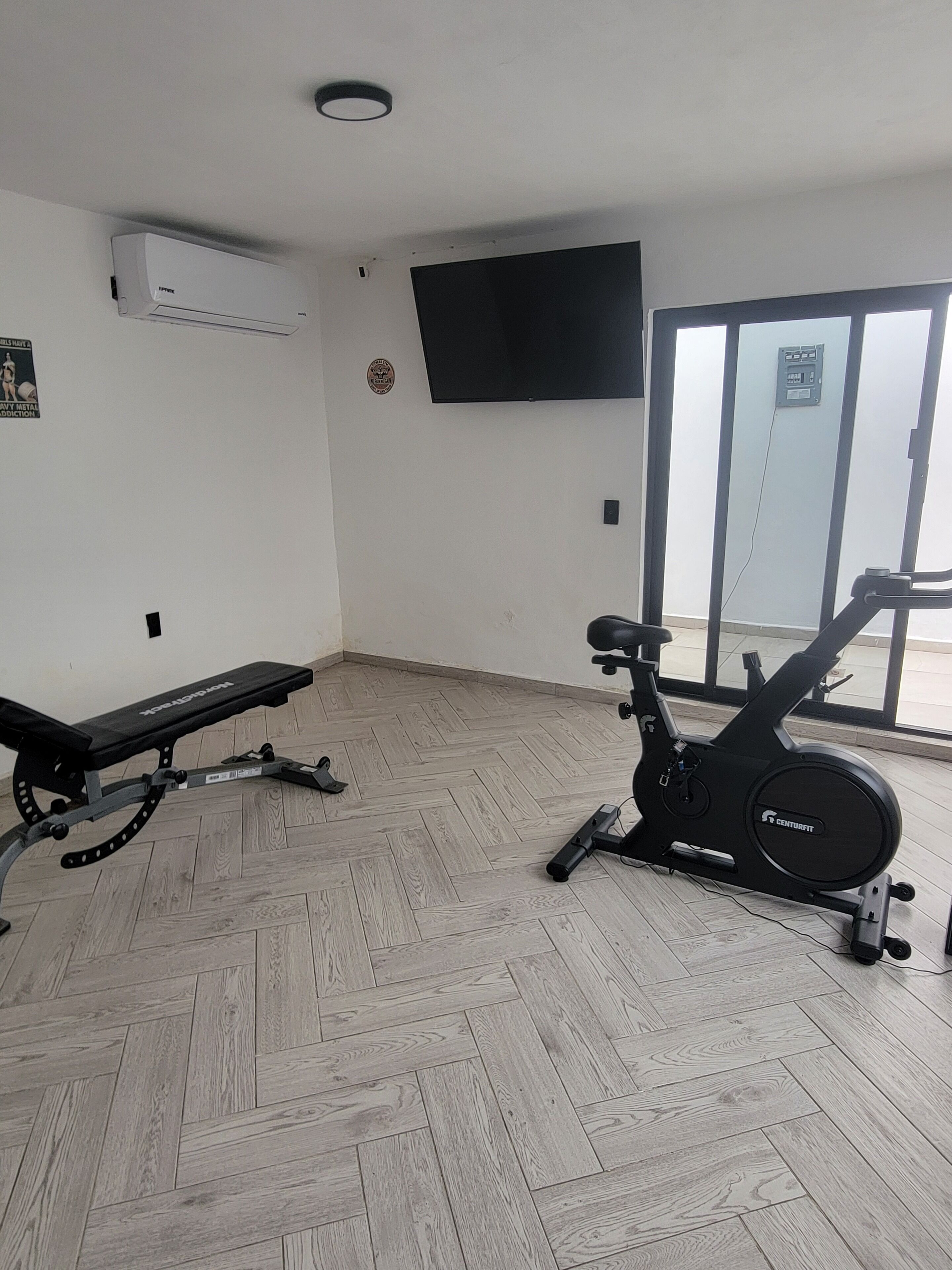 A gym with a stationary bike, a bench, and a television on the wall.