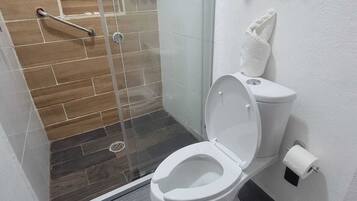 Un baño moderno con ducha de vidrio, inodoro blanco y un perchero para toallas.