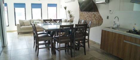 Una cocina moderna con comedor, que incluye una mesa grande, sillas, estufa integrada y un televisor montado en la pared.