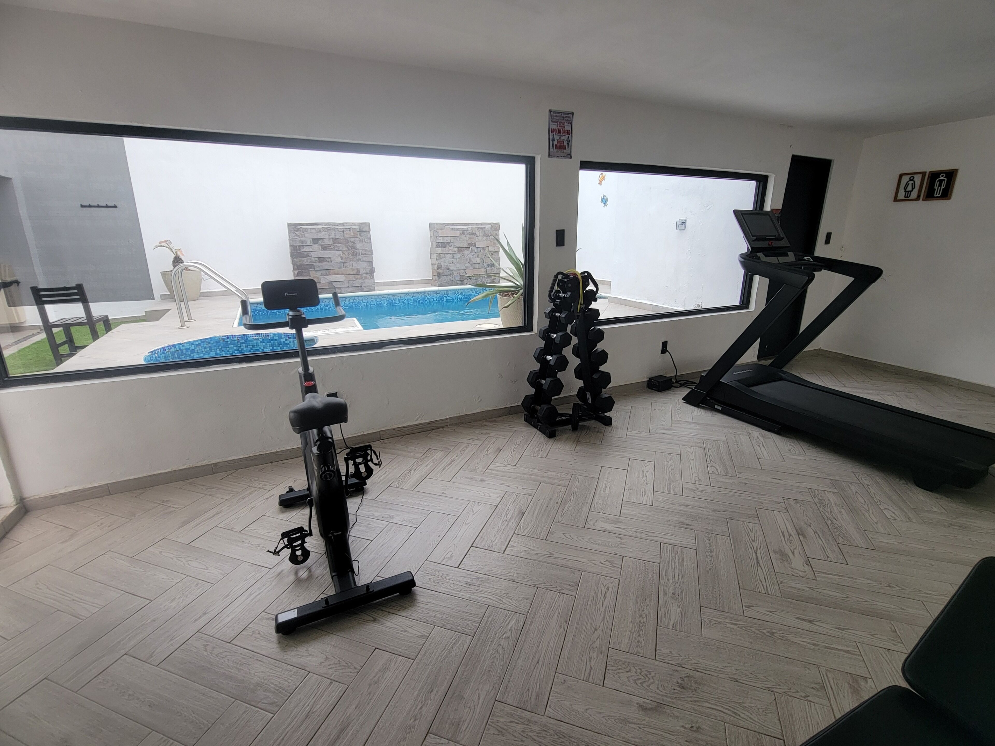 A home gym with exercise equipment, a treadmill, and a view of a swimming pool.