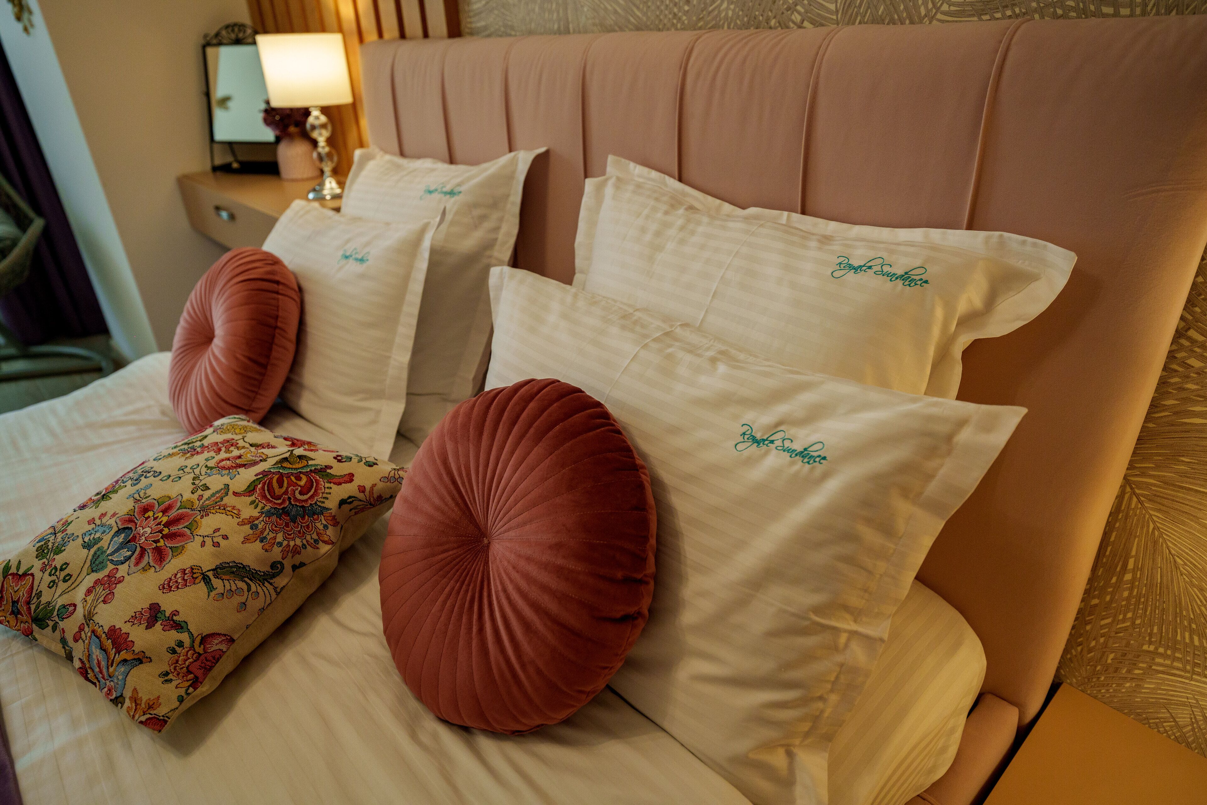 Ein Bett mit zahlreichen Kissen, darunter eines mit Blumenmuster und mehrere mit Stickereien.