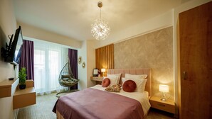Ein modernes Hotelzimmer mit einem großen Bett, einem Fernseher, einem Sessel und einem Schreibtisch mit Lampe.