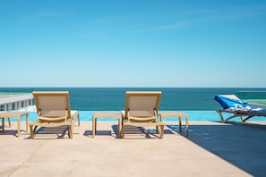A poolside area with lounge chairs and a view of the ocean.