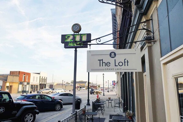 Une vue de rue avec une enseigne indiquant l’hôtel « The Loft », une horloge et des voitures garées.