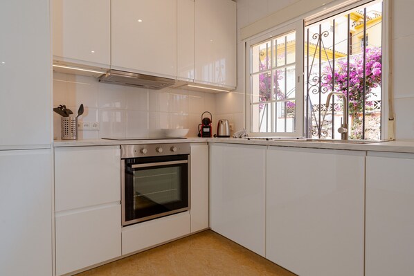 Una cocina con armarios blancos, un horno de acero inoxidable, una cafetera y una ventana con vistas a flores rosadas.