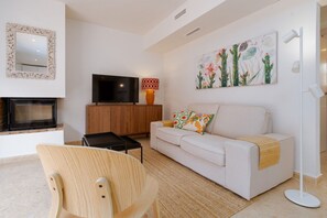 A modern living room with a sofa, a television, a fireplace, and a cactus painting.