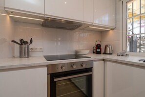 Cocina moderna con armarios blancos, placa de inducción negra, horno de acero inoxidable y ventana con reja decorativa.