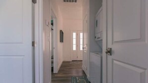 A hallway with white doors, a wooden floor, and a green 'Laundry' mat at the end. - Two Bedroom Farmhouse Cottage No. 2
 (Orderville)