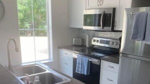 A modern kitchen with white cabinets, stainless steel appliances, and a large window providing natural light. - Two Bedroom Farmhouse Cottage No. 2
 (Orderville)