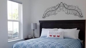 A bedroom with a bed, a nightstand, a lamp, a window, and a decorative wall piece. - Two Bedroom Farmhouse Cottage No. 3
 (Orderville)