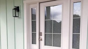 A white front door with a glass panel, a black doormat, and a wall-mounted light fixture. - Two Bedroom Farmhouse Cottage No. 3
 (Orderville)