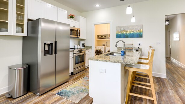 A modern kitchen with stainless steel appliances, white cabinetry, and a central island with bar stools. - Chic Thomasville Home: Walk to Downtown! (Thomasville)