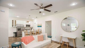 A modern living room with a white sofa, coffee table, and a desk with a chair. A ceiling fan and recessed lighting are visible. - Chic Thomasville Home: Walk to Downtown! (Thomasville)