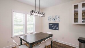 A dining area with a wooden table, white chairs, a hanging light fixture, and a chalkboard with a message. - Chic Thomasville Home: Walk to Downtown! (Thomasville)