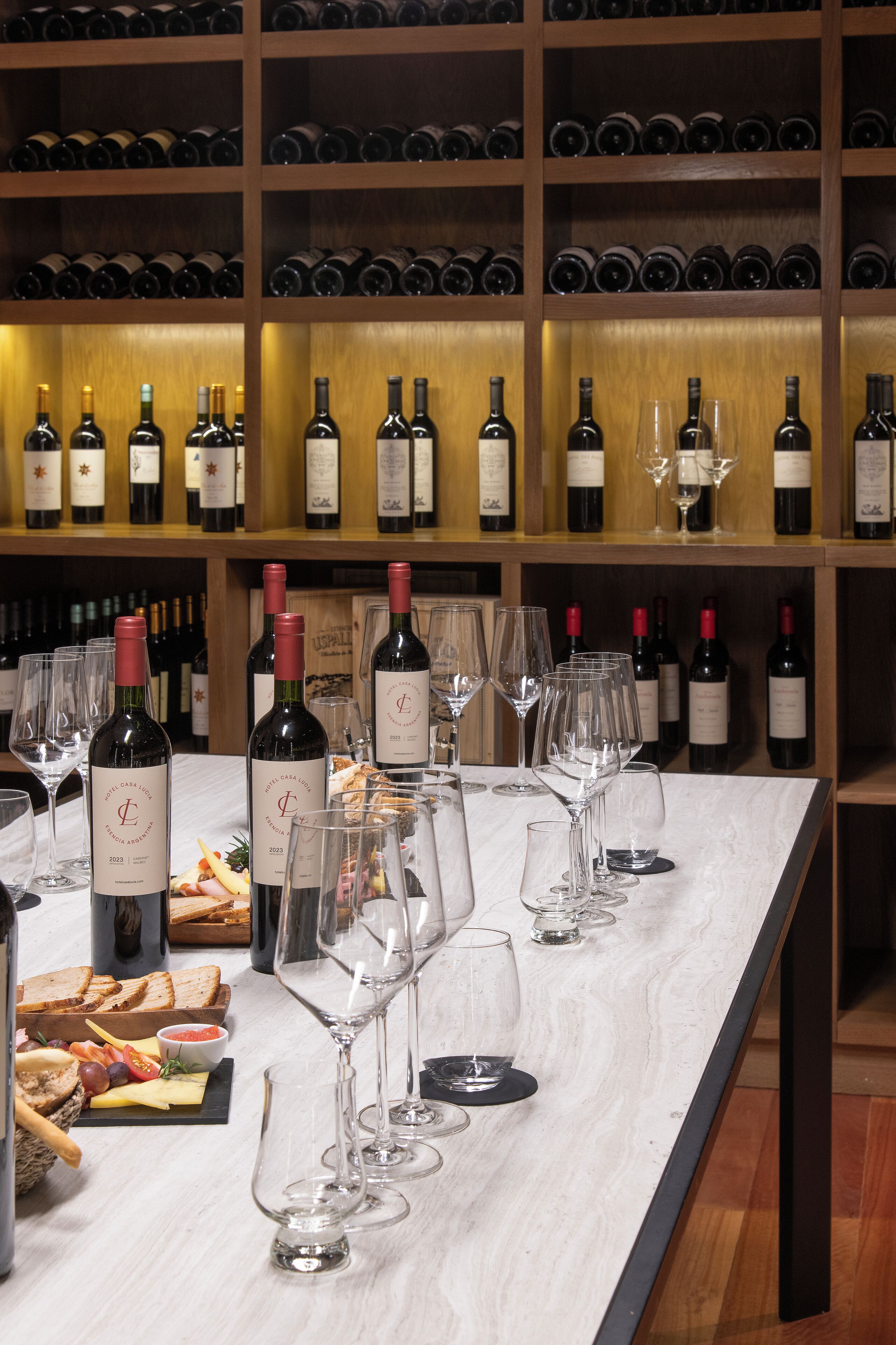 Disposición para cata de vinos con botellas y copas sobre una encimera de mármol, rodeado de estanterías llenas de botellas.