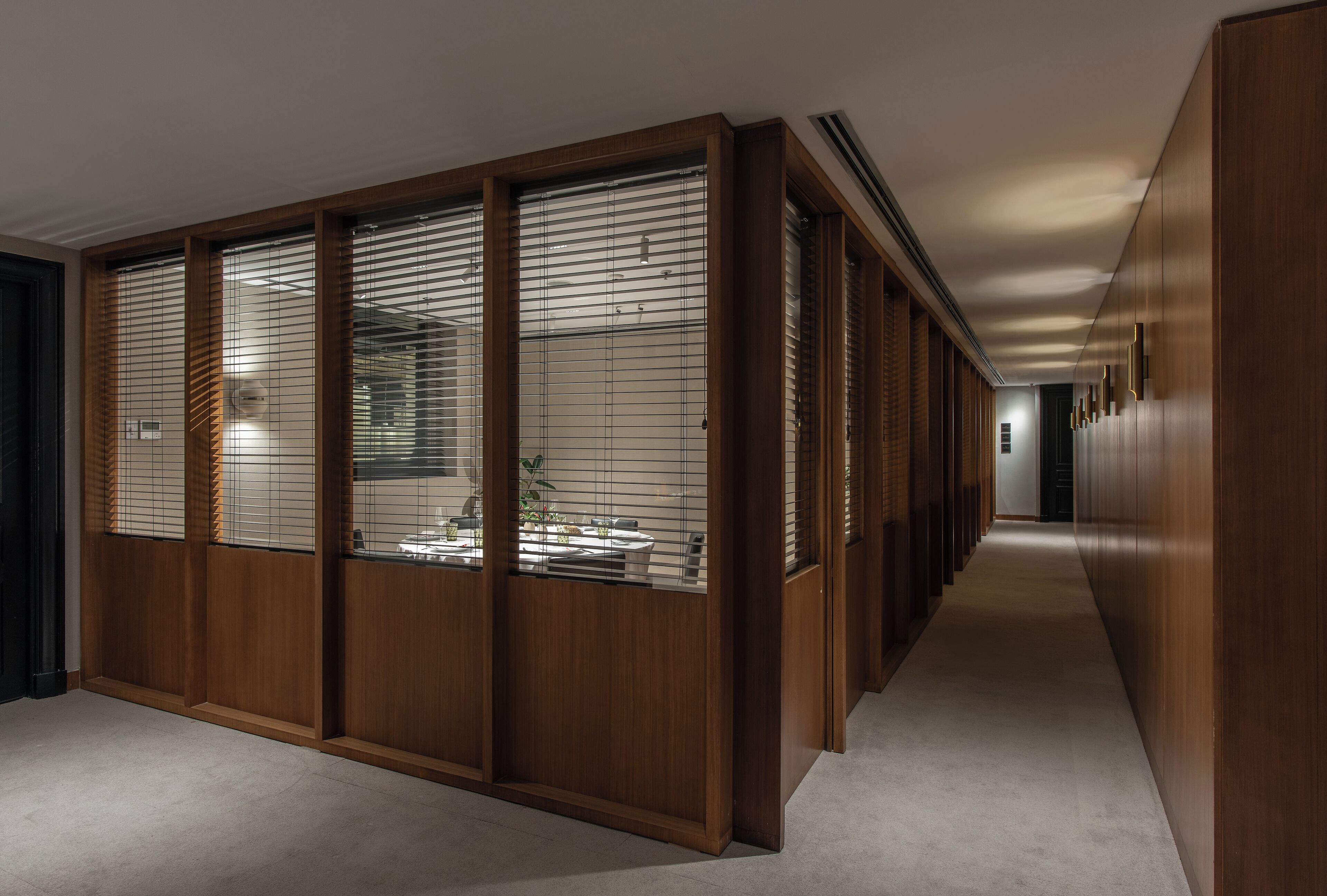 A corridor with wooden paneling and sliding glass doors, leading to a room with a bed and a nightstand.